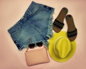 Vystaveny fotografie. Letní sada oblečení na růžovém pozadí tvořené džínové šortky, žlutá čepice, brýle a kosmetická taška a žabky