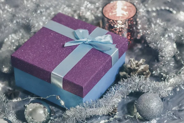 Shiny gift box with gift and holiday decorations on gray background.