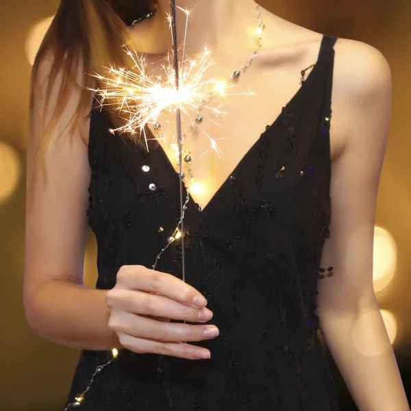 Junges Mädchen im Abendkleid hält eine brennende Wunderkerze auf verschwommenem Goldgrund mit Bokeh — Stockfoto