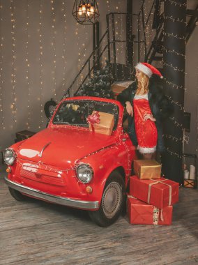 Şenlikli dekorasyonların arka planında genç ve güzel bir kar kızı ve hediyeli kırmızı bir araba ve Noel ağacı.