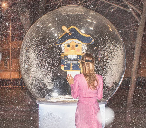 Balle magique avec un casse-noisette à l'intérieur et une fille de ballerine dans une robe rose brillant à côté sur un fond neigeux — Photo