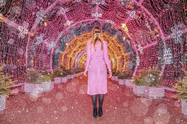 Young girl in a pink dress on the background of a multi-colored glowing tunnel in a snowy evening, Moscow, Russia — Stock Photo, Image