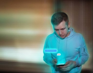 A young guy with a phone in his hands writes a message to his girlfriend in the evening at home. Blue neon light.