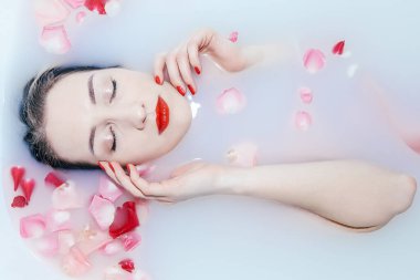 Genç seksi kız gül yapraklarıyla süt banyosu yapıyor.
