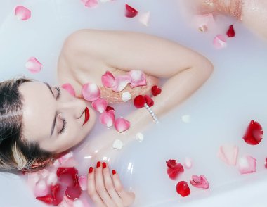 Genç seksi kız gül yapraklarıyla süt banyosu yapıyor.