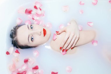 Genç seksi kız gül yapraklarıyla süt banyosu yapıyor.