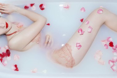 Genç seksi kız gül yapraklarıyla süt banyosu yapıyor.