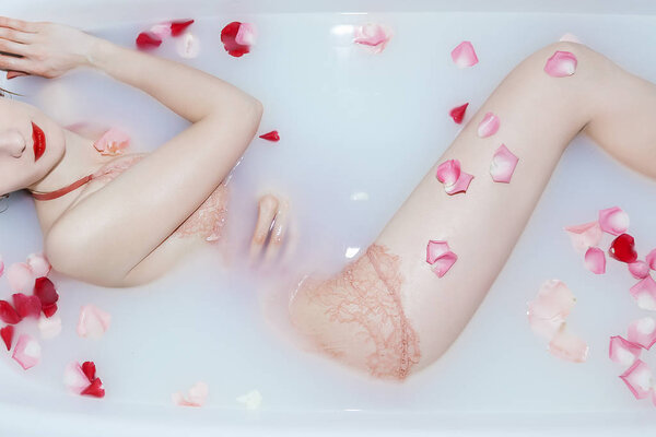 Young sexy girl taking a milk bath with rose petals