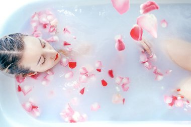 Genç seksi kız, gül yapraklarıyla süt banyosu yapıyor.