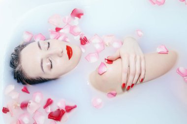 Genç seksi kız, gül yapraklarıyla süt banyosu yapıyor.