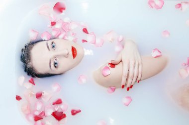 Genç seksi kız, gül yapraklarıyla süt banyosu yapıyor.