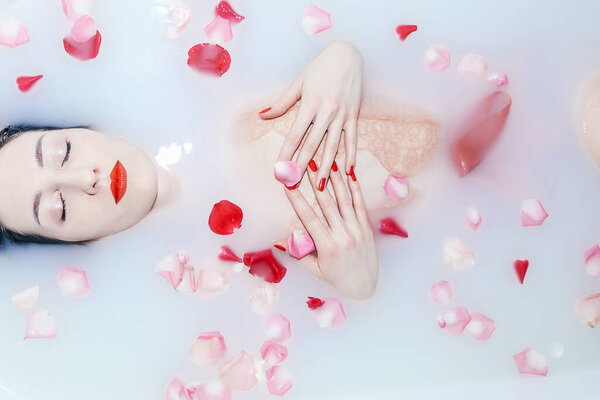 Молодая сексуальная девушка принимает молочную ванну с лепестками роз крупным планом
