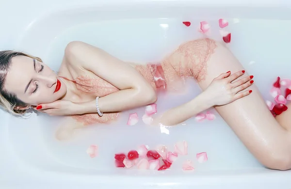 Giovane ragazza sexy che prende un bagno di latte con petali di rosa primo piano — Foto Stock