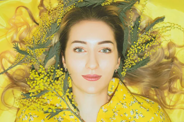 Portrait of young pretty woman with mimosa on the yellow background closeup.