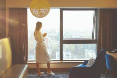 Sarı gündoğumu saatinde, otel penceresinde beyaz bornozlu bir fincan kahveyle genç ve güzel bir kadının silueti..