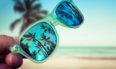 Güneş gözlüğü el kumsalda tutan adam