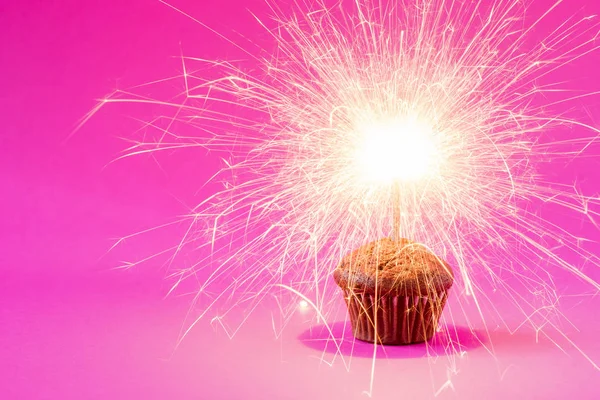 Cupcake with a sparkler over a pink background. — Stock Photo, Image