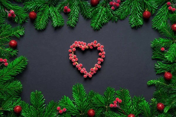 Noel çerçevesi Wirh köknar dalı, böğürtlen kalbi ve siyah arka planda takılar — Stok fotoğraf