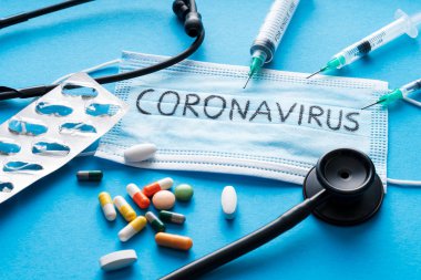 Mavi arka planda koruyucu yüz maskesi, haplar, şırıngalar ve steteskop, Novel Coronavirus 2019-ncov veya Wuhan Coronavirus 'a karşı. Hijyen ve Sağlık Hizmetleri kavramı