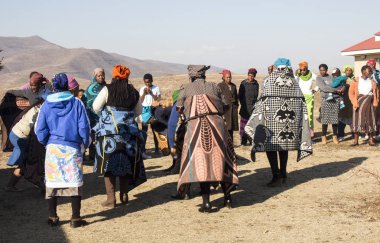 African women Bantu nation Basotho tribe in modern handmade traditional colorful blankets are standing in the village and talking to each others. Tribal meeting. clipart