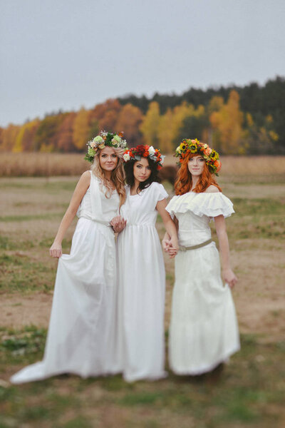 three colors of autumn. three girls in autumn wreaths stand on nature