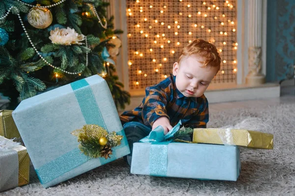 Petit garçon assis près des boîtes et l'ouverture des cadeaux de Noël — Photo