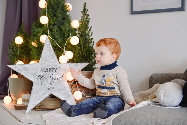 Petit garçon assis près des lumières de Noël près de l'arbre — Photo