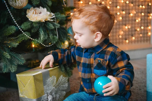 Petit garçon assis près des boîtes et l'ouverture des cadeaux de Noël — Photo