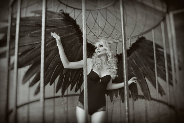 blond woman with black wings in a cage. Angel, mysticism