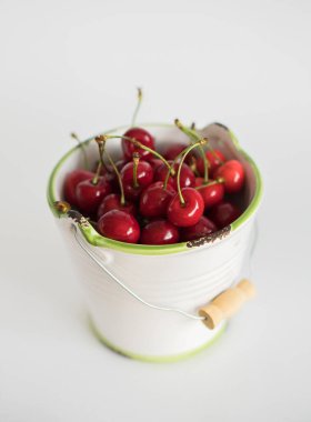 Beyaz arka planda yeşil kenarı olan beyaz bahçe diş minesi kovasında olgun kırmızı kiraz.