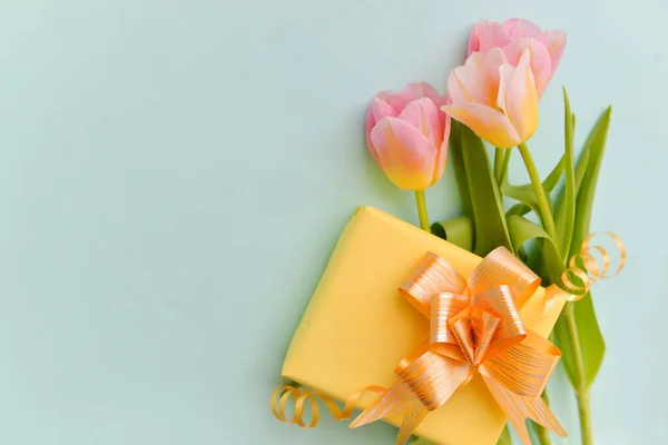 Buquê de tulipas delicadas e um presente caixa amarela com um arco brilhante em um fundo azul isolado, arranjo festivo floral de flores, paillettes doces de ouro contra o fundo Imagens De Bancos De Imagens