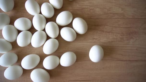 Крутящееся вареное яйцо в группе белых куриных яиц на деревянном столе — стоковое видео