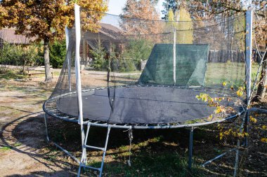 Ön bahçenin ön bahçesinde trambolin. Ağaçların yanında trambolin. Etrafta altın meşe yaprakları var. Sonbahar yapraklarında oyun parkı