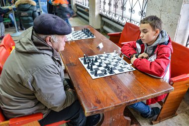 Torun ve büyükbaba satranç oynuyorlar. Öğrenciler arasında satranç turnuvası. Çocuklar satranç oynar. Karnaval kutlaması. Bilogorotka. Ukrayna. Shrovetide, 25 Şubat 2017