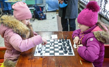 İki kız satranç oynuyor. Kızlar başlarını tahtaya eğdiler. Öğrenciler arasında satranç turnuvası. Çocuklar satranç oynar. Karnaval kutlaması. Bilogorotka. Ukrayna. Shrovetide, 25 Şubat 2017