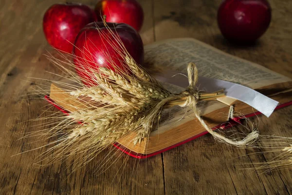 Maçã e espigas de trigo no livro em um fundo embaçado — Fotografia de Stock