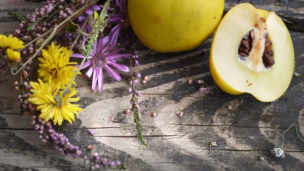 Maturare mele cotogne e mazzo di fiori selvatici su tavolo di legno grezzo. Tema romantico con arredamento naturale . — Foto Stock