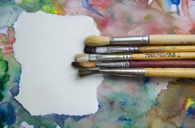 A group of paintbrushes on abstract colorful watercolor background with place for text. Can be used for background, banner, poster, advertising workshops. Blank for motivating quote, note, message. clipart