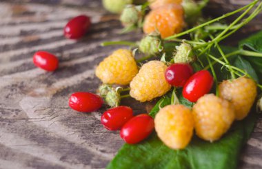 Ahududu ve kenan sarı meyve ile eski dokulu ahşap arka plan üzerinde yapraklar. Organik çilek portre. Olgun taze beyaz ahududu ve kızılcık.