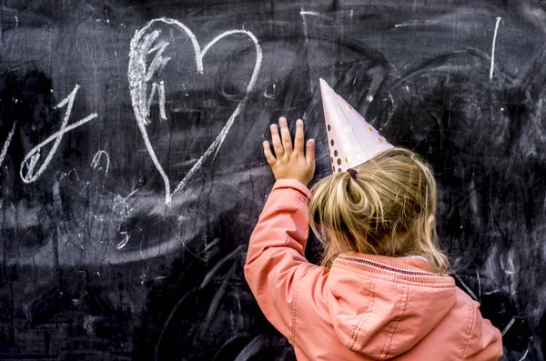 Tatil şapkalı bir kız Tebeşirle bir kalp çizer.