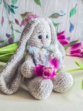 Açık gri el yapımı, pembe laleli bir tavşan. Çocuk oyuncağı. Tığ işi deseni. El işi üretimi..