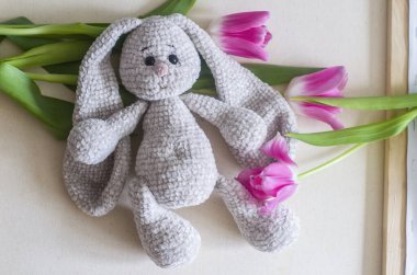 Açık gri el yapımı, pembe laleli bir tavşan. Çocuk oyuncağı. Tığ işi deseni. El işi üretimi..