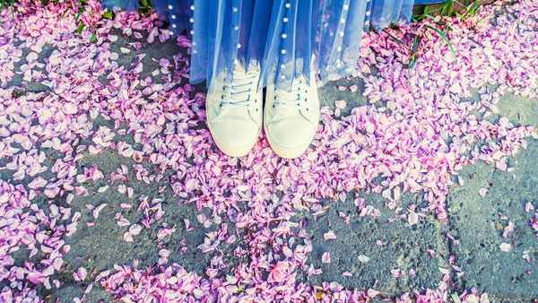 White sneakers and blue skirt. Top view of sakura petals on asphalt. Photo banner.