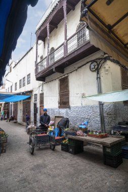 Meyve ve sebze tezgahlarının arasında arabası olan bir adam. 