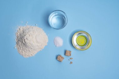 Ekmek yapmak için gereken malzemeler renkli bir yüzeye yerleştirilmiş ve yukarıdan çekilmiş.