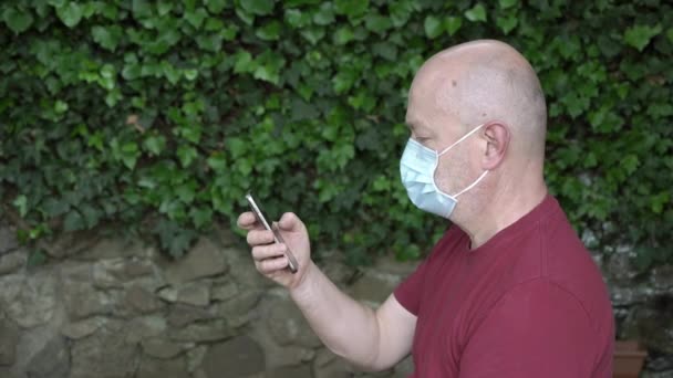 コヴィト19回で彼のスマートフォンにメッセージを書きながら保護マスクを持つ男 — ストック動画