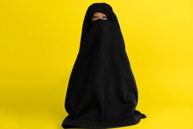 Siyah bornozlu, sarı arka planda yüzü kapalı bir bebek.