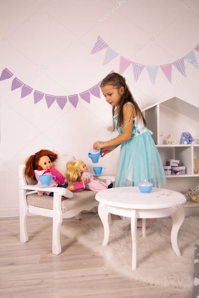 small elegant caucasian girl in a blue dress play with dolls, tea party with toys