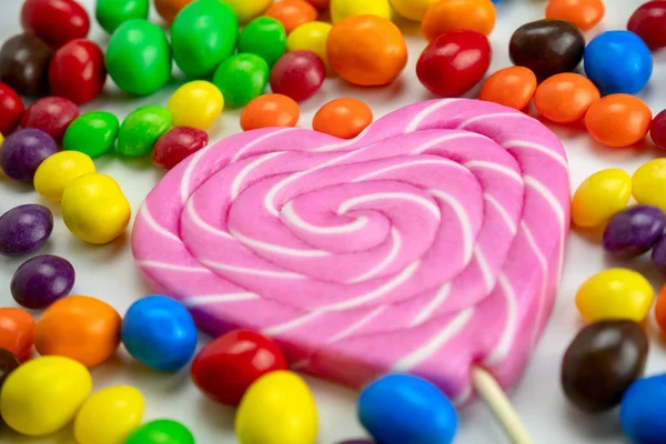 色彩艳丽的糖果和白色背景的粉色棒棒糖使我们的注意力更加集中 不健康的饮食和孩子们的聚会食物概念更加引人注目 — 图库照片