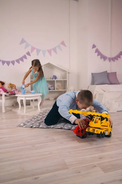 Güzel, mutlu, beyaz çocuklar odalarında oynuyorlar. Oğlan arabalarla oynuyor, kız bebeklerle oynuyor.